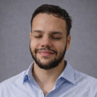 Retrato de Lucas Tito, de camisa azul-clara diante de um fundo cinza.